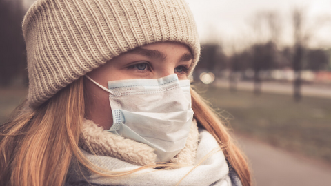 Many people have breathing problems in the winter. Lung specialist Prof. Fischer give tips on how to protect your lungs from the cold, dry air and fine dust. Young woman wearing a scarf, hat and face mask standing at a bus stop