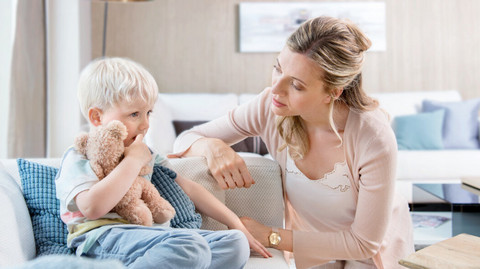 What can be done if a child has mucus in their throat? 8 easy tips for parents Kleiner Junge sitzt mit Kuscheltier auf der Couch, Mutter sitzt besorgt davor