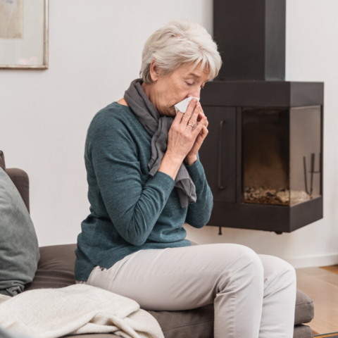 Mucus in patients with COPD and bronchiectasis: Interview with Prof. Fischer Ältere Frau sitzt auf der Couch im Wohnzimmer und putzt sich die Nase