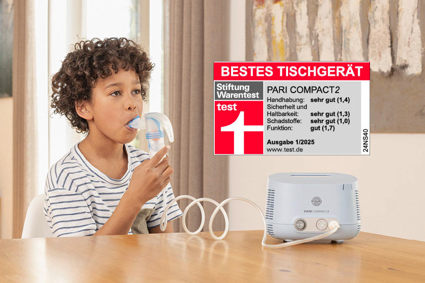 Ein Kind inhaliert mit einem PARI COMPACT2 Inhalator Ein Kind inhaliert mit einem blauen PARI COMPACT2 Inhalator, während der Vater unterstützend daneben sitzt.