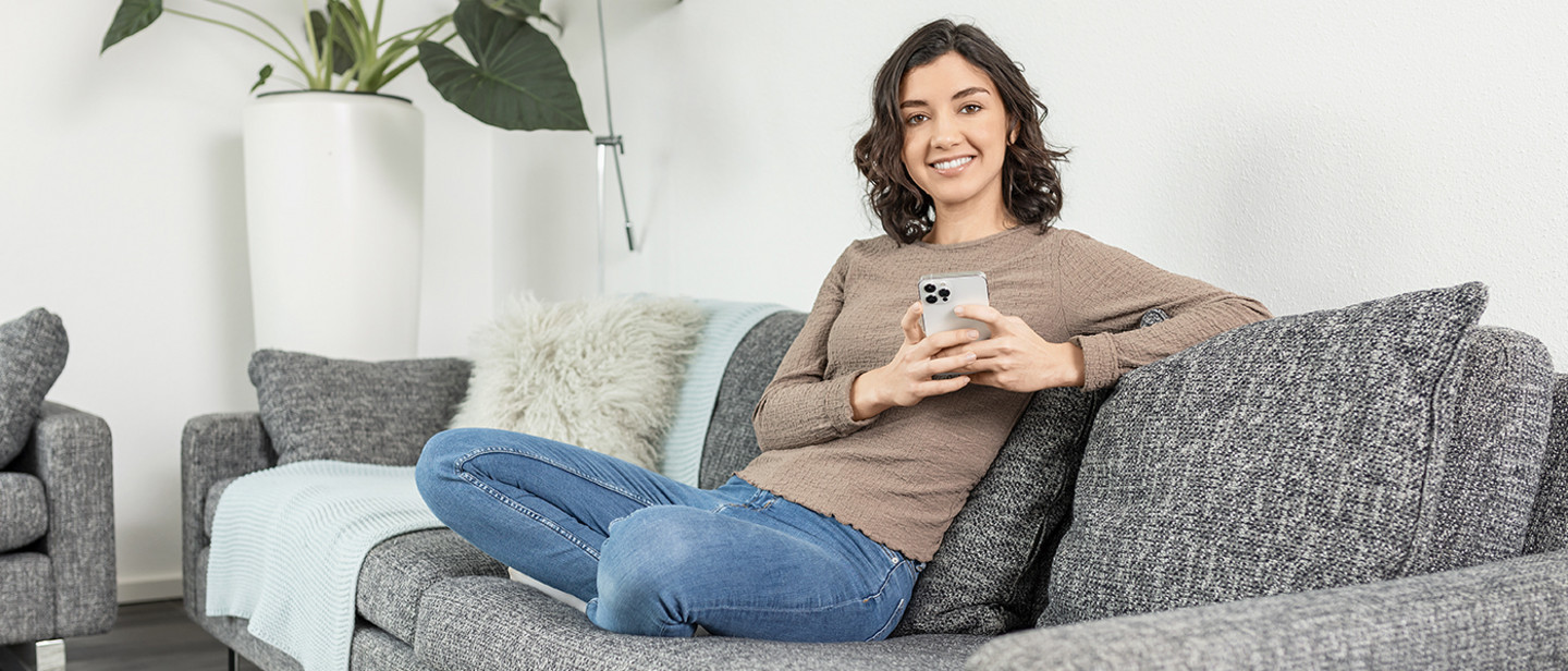 PARI Blog A person sits relaxed on the sofa, holding a smartphone and a cup in the living room.