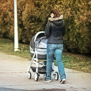 Junge Frau mit Kinderwagen beim Spaziergang von hinten