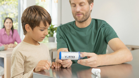 Spacer inhalation with children: Instructions & the suitable equipment Father sits with his son at the kitchen table and shows him the VORTEX spacer