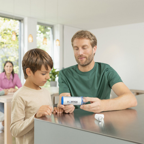 Spacer-Inhalation mit Kindern: Anleitung & das passende Equipment Vater sitzt mit Sohn am Küchentisch und zeigt ihm die VORTEX Inhalierhilfe