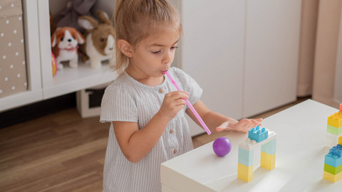 Games for children to expel mucus from the lungs: 3 simple ideas Kleines Mädchen kniet vor Spieltisch und bläst Ball mit Strohhalm durch kleine Duplo-Tore