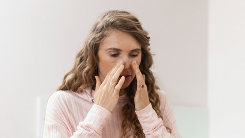 Side effects of a nasal douche – and how to avoid them Young woman holding both hands at the top of her nose