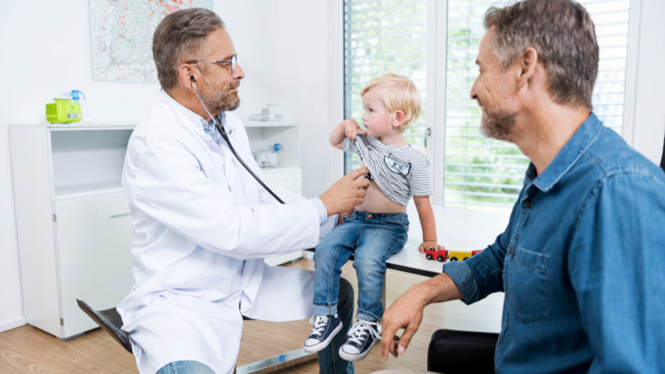 Coughing in children: What can help if your child has a lung infection? Doctor examining little boy with father sitting next to them, watching