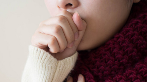 Tips: Coughing properly when your airways are irritated and your lungs are full of mucus Frau hustet in die geschlossene Faust, die andere Hand hält sie sich an den Hals