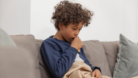 If your child is constantly coughing: This is how your child can learn to control the urge to cough and to cough properly Boy sitting on the couch coughing