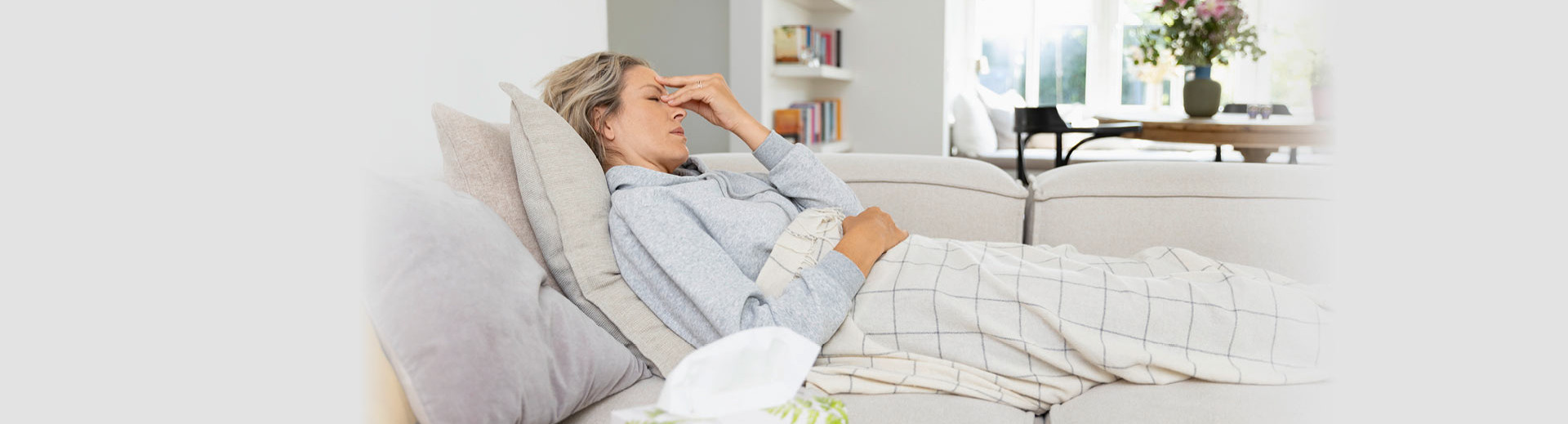 Woman lies sick on the sofa and holds her head