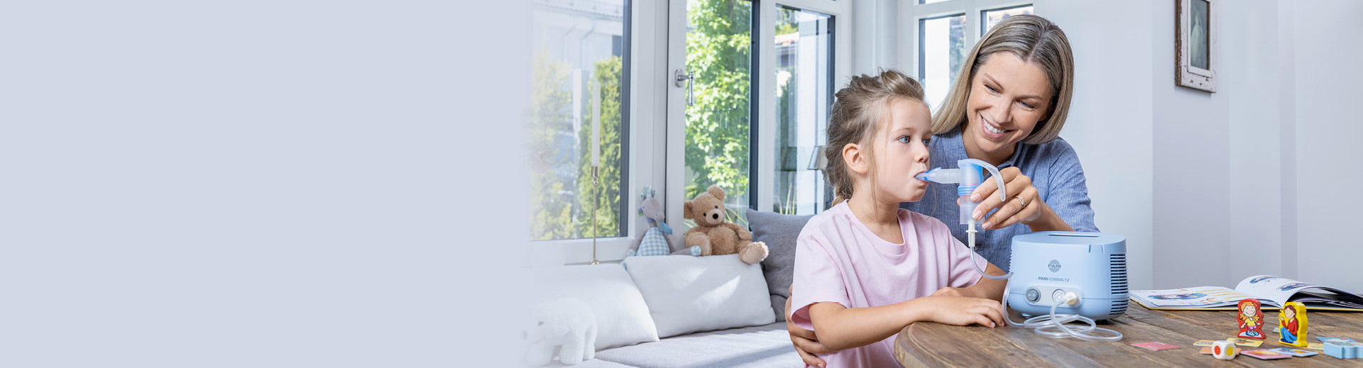 A young mother helps her daughter inhale with a PARI Compact2 inhalation device