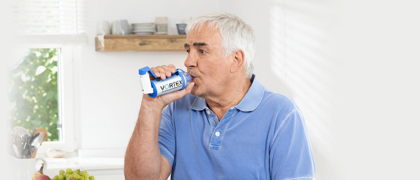 Inhalation therapy with asthma spray Older man in a light blue polo shirt using an asthma spray in a bright kitchen setting.