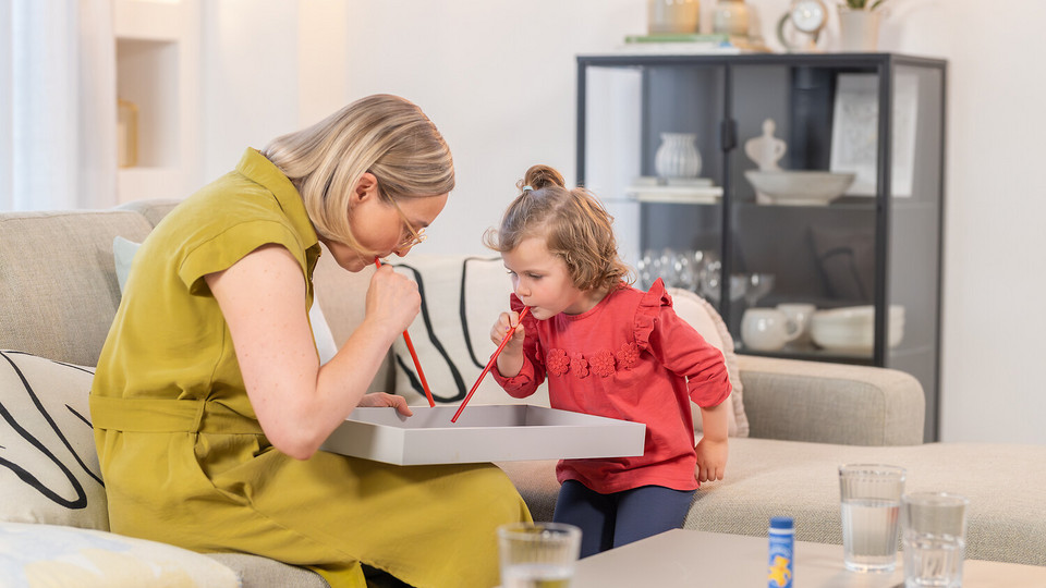 Games for children to expel mucus from the lungs: 3 simple ideas Young woman sitting on the couch with daughter playing blowing games