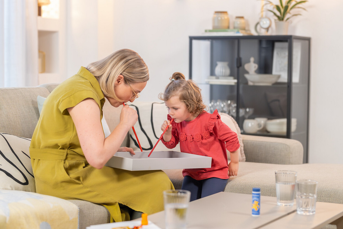 Games for children to expel mucus from the lungs: Blowing games Young woman sitting on the couch with daughter playing blowing games
