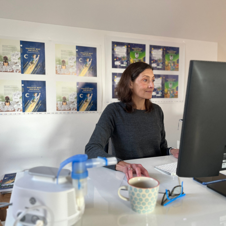 What can you do if your voice is hoarse? An author explains how she keeps her voice fit for public readings Junge Frau sitzt vor Computer am Schreibtisch, im Vordergrund ist unscharf ein Inhalationsgerät zu erkennen