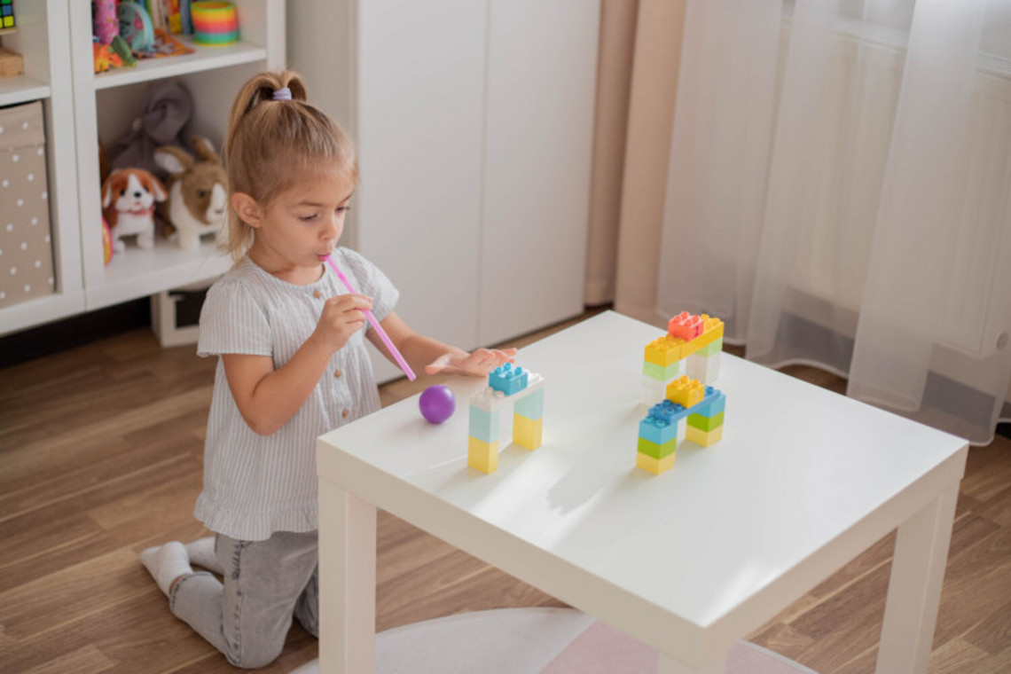 Games for children to expel mucus from the lungs: Blowing games Little girl kneels in front of play table and blows balls over it with a straw