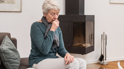 Dry cough (tickly cough): Causes and home remedies Ältere Frau sitzt im Wohnzimmer auf der Couch und hustet in die geschlossene Faust