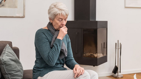 Tips: Coughing properly when your airways are irritated and your lungs are full of mucus Eldery woman sitting on the couch in the living room coughing