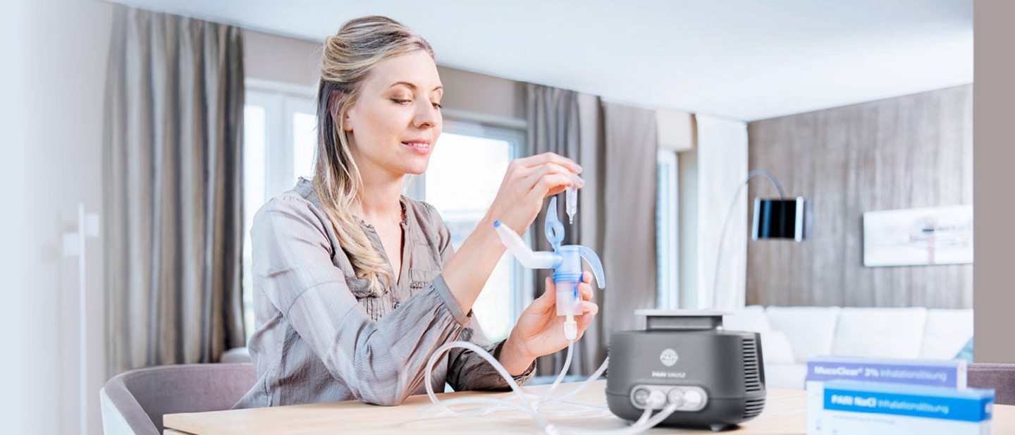 Products that can be used for inhalation Young woman sitting at a table in a bright room filling a nebuliser attached to an inhalation device with saline solution.