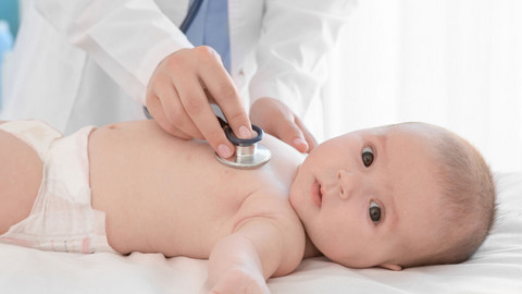 Coughs and colds in infants: How your baby can gently get over the infection Säugling liegt auf Liege und schaut in die Kamera, Arzt hält Stethoskop auf seine Brust