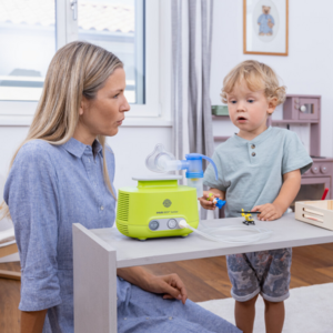 Young mother sitting at the table in the nursery, her young son standing next to her, a PARI BOY inhalation device on the table