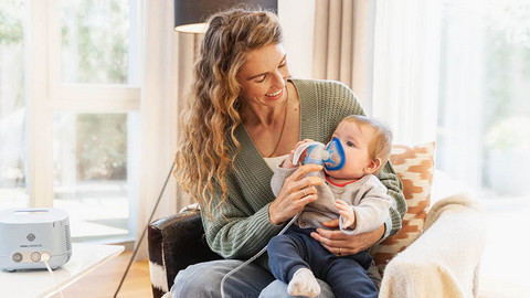 Inhalieren mit Säugling Junge Mutter hat Baby auf dem Schoß, Baby inhaliert mit Vernebler und Maske