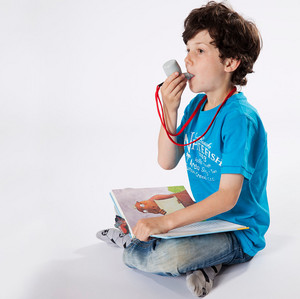 Child sits cross-legged on the floor with an open book on their lap, breathing through the PARI O-PEP respiratory therapy device