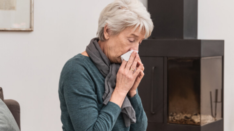 Mucus in patients with COPD and bronchiectasis: Interview with Prof. Fischer Ältere Frau sitzt auf der Couch im Wohnzimmer und putzt sich die Nase