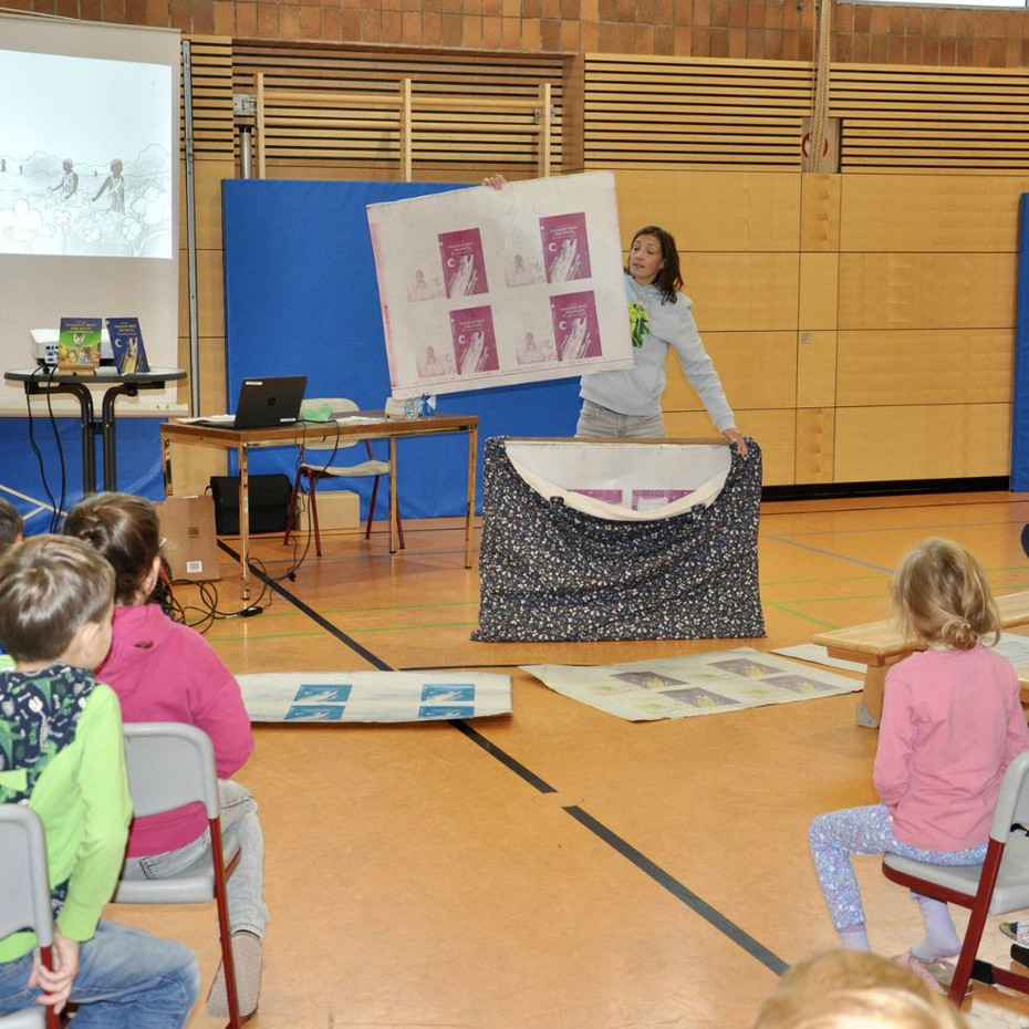 What to do with a hoarse voice: Author Alexandra Wagner during a reading Author stands in front of seated children in the gym and holds up the printing plates of her book