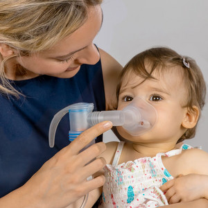 Nahaufnahme einer jungen Mutter, die ihrem Baby einen Vernebler mit Babymaske und Babywinkel vors Gesicht hält