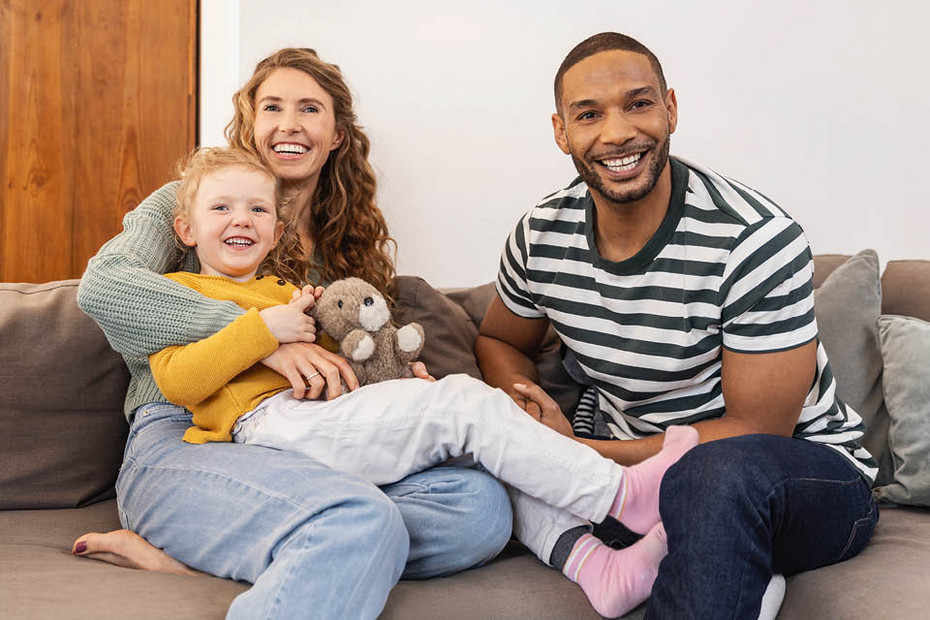Children need positive inhalation experiences Mother and father sitting on a sofa with a young child on their lap holding a plush toy, all seated close together.