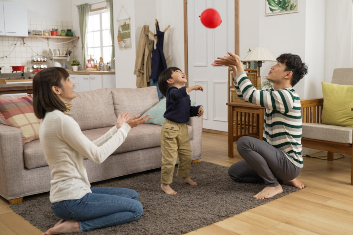 Games for children to expel mucus from the lungs: Balloon game Mother, father and little son playing with balloon on the living room floor