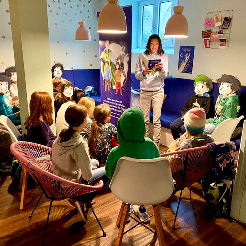 Autorin Alexandra Wagner liest in einem Café aus ihrem Buch, vor ihr sitzen Kinder und hören gespannt zu