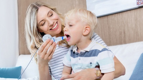 Inhalation therapy with cystic fibrosis despite taking CFTR modulators? Cystic fibrosis patients address the question Junge Mutter hat kleinen Sohn auf dem Schoß und hilft ihm beim Inhalieren