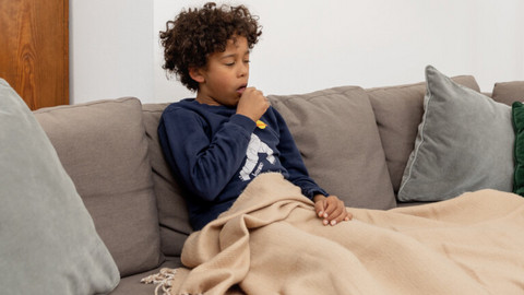 Warum hustet man? Einfache Erklärung für Kinder Junge sitzt auf Couch mit Decke und hustet in die Faust