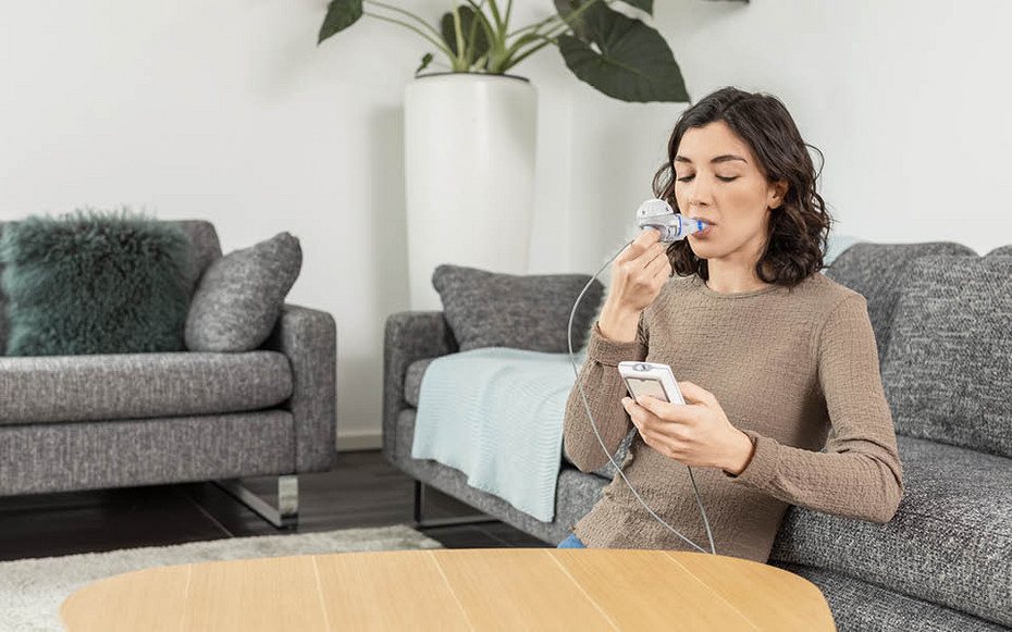 Inhalation in cystic fibrosis is important Mother seated on a sofa holding a young child on her lap while helping the child use a nebuliser connected to an inhalation device.