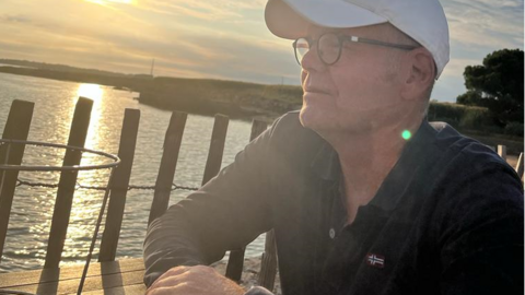 Tag der Seltenen Erkrankungen: Rezidivierende Polychondritis – Interview mit Hans-Martin Schühle Mann sitzt an einem Tisch am Seeufer und schaut hinaus auf den See