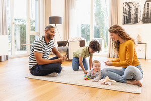 Vater und Mutter sitzen mit ihrem Sohn und ihrem Baby auf dem Teppich und spielen