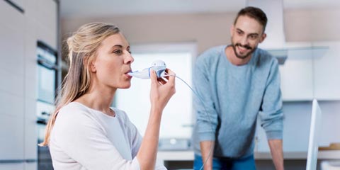 Eine Frau benutzt ein Inhalationsgerät, während ein Mann lächelnd daneben steht.