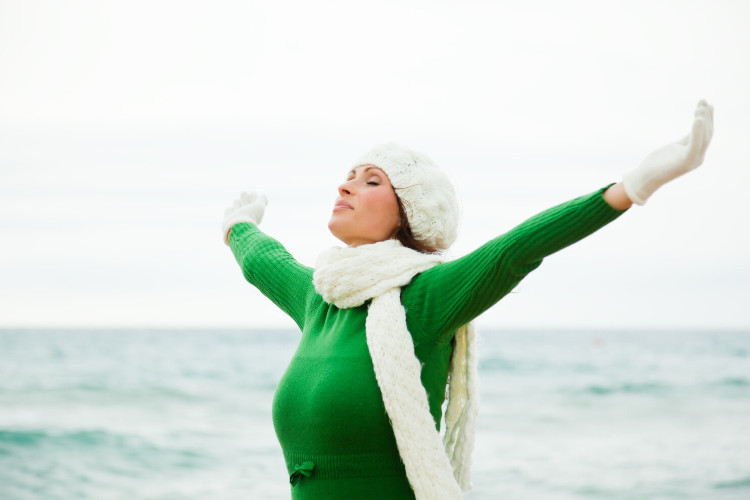 Breathing through your nose warms the air Young woman with beanie and scarf and arms outstretched breathing sea air