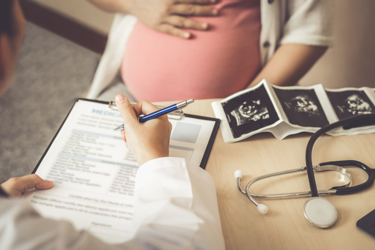Pregnancy with cystic fibrosis: at the gynaecologist A doctor's hand fills out a questionnaire, the belly of a pregnant woman can be seen in the background