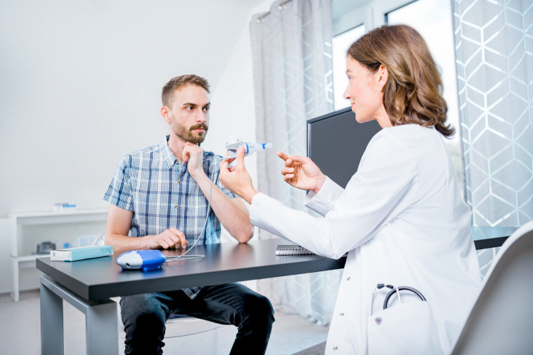 Ccystic fibrosis therapy and CFTR modulators: Consultation with physician Young man sits opposite doctor who explains inhalation device to him