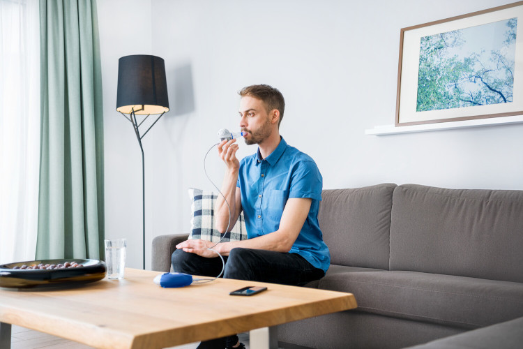 Cystic fibrosis therapy and CFTR modulators: Inhalation Young man sits on couch and inhales with inhalation device
