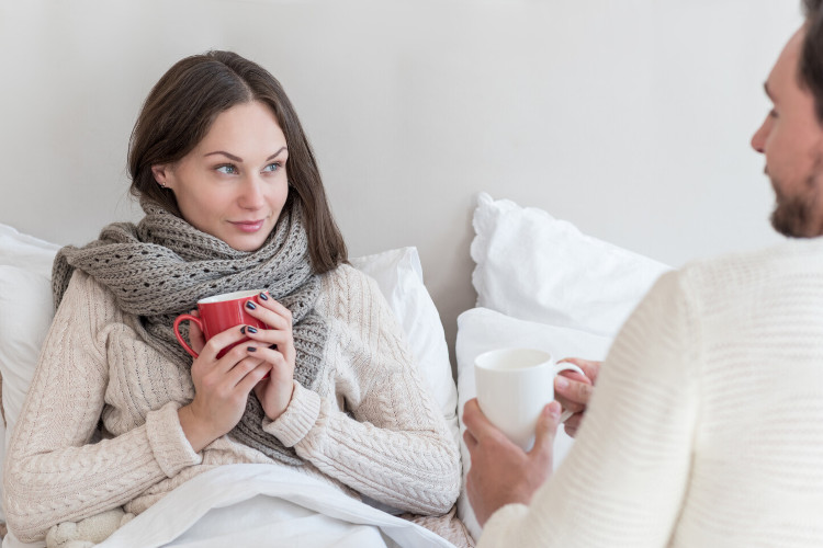 Painful cough: Drink warm tea Young, sick woman sits in bed and drinks tea
