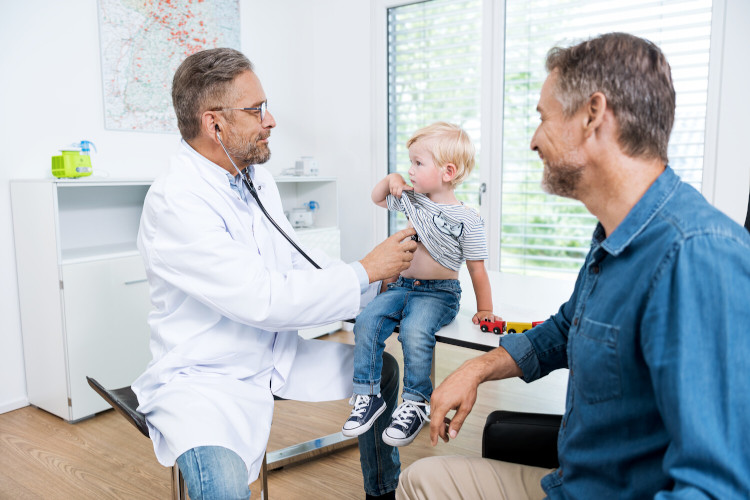 Coughing in children: At what point do you go to the doctor? Doctor examines young child with stethoscope while father sits next to them