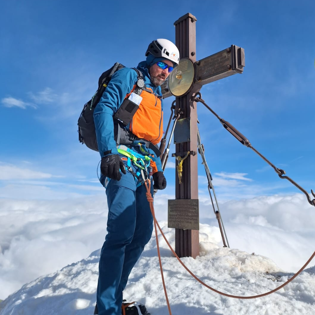 Mann steht an schneebedecktem Gipfelkreuz