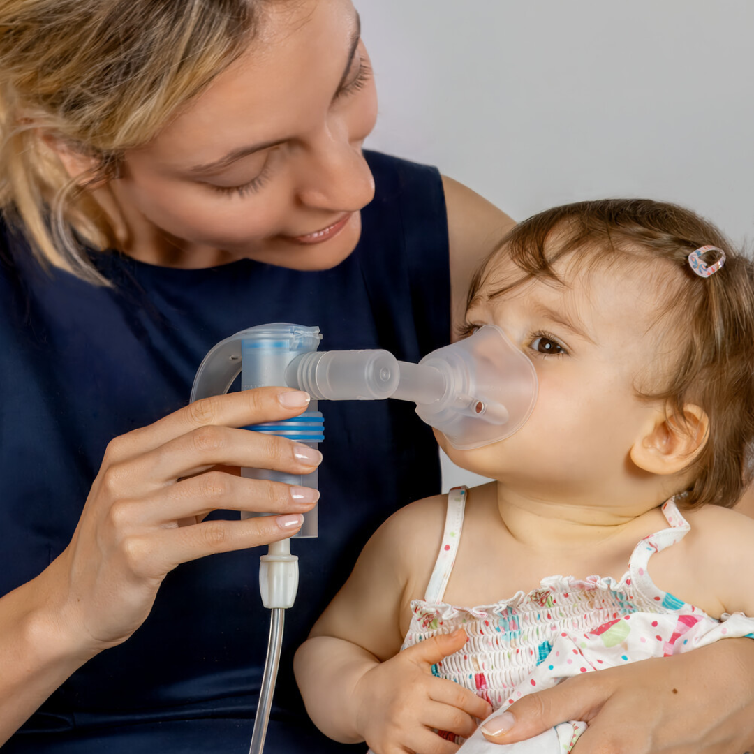 Nahaufnahme von Mutter mit Baby auf dem Schoß, Mutter hat PARI Vernebler in der Hand und hält die Maske vor das Gesicht das Babys