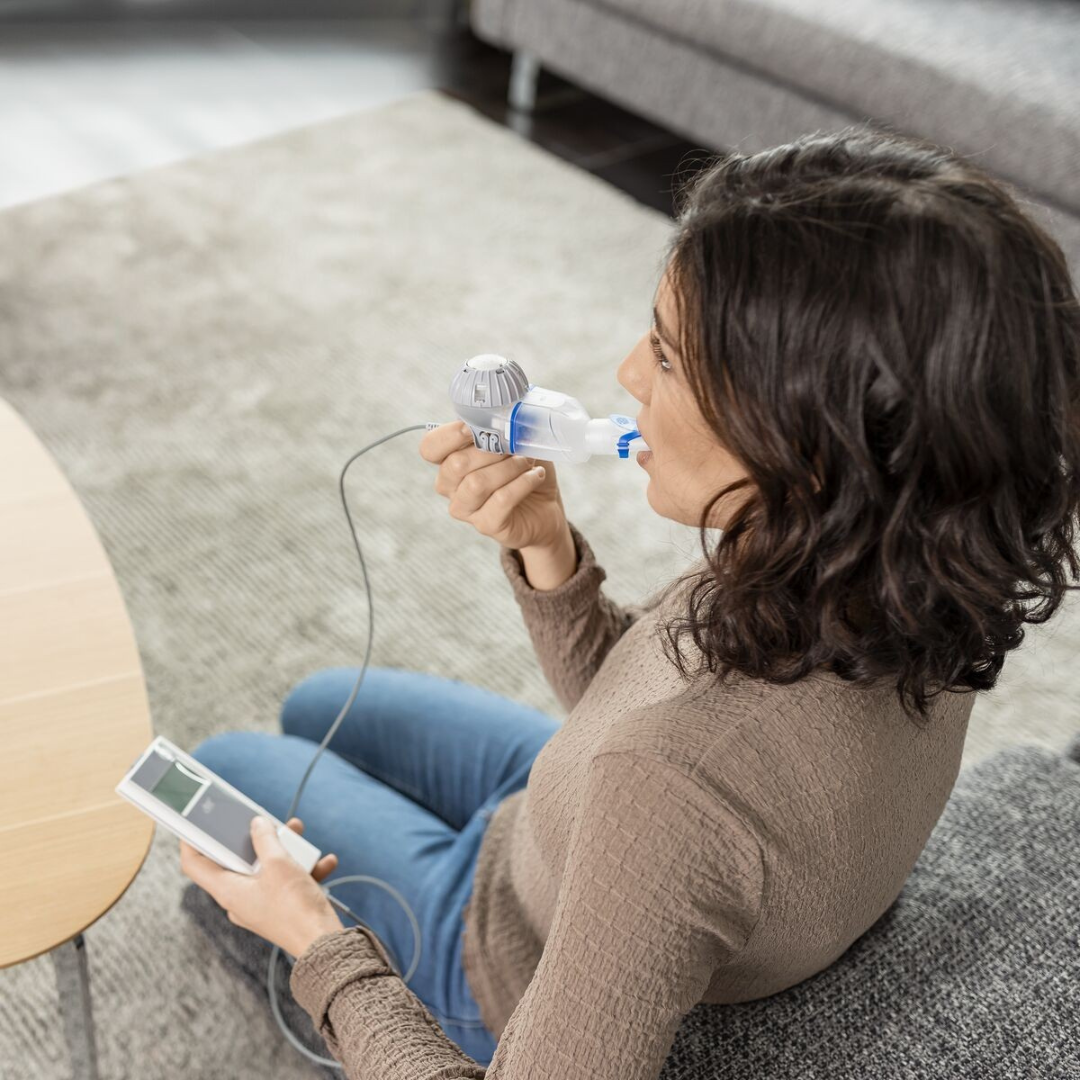 Aufnahme einer jungen Frau seitlich von hinten, die mit dem eFlow rapid Inhalationssystem mit eTrack Controller inhaliert