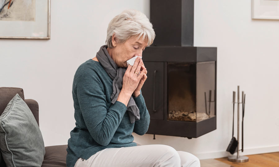 A woman with a cold sits on the sofa and cleans her nose with a handkerchief