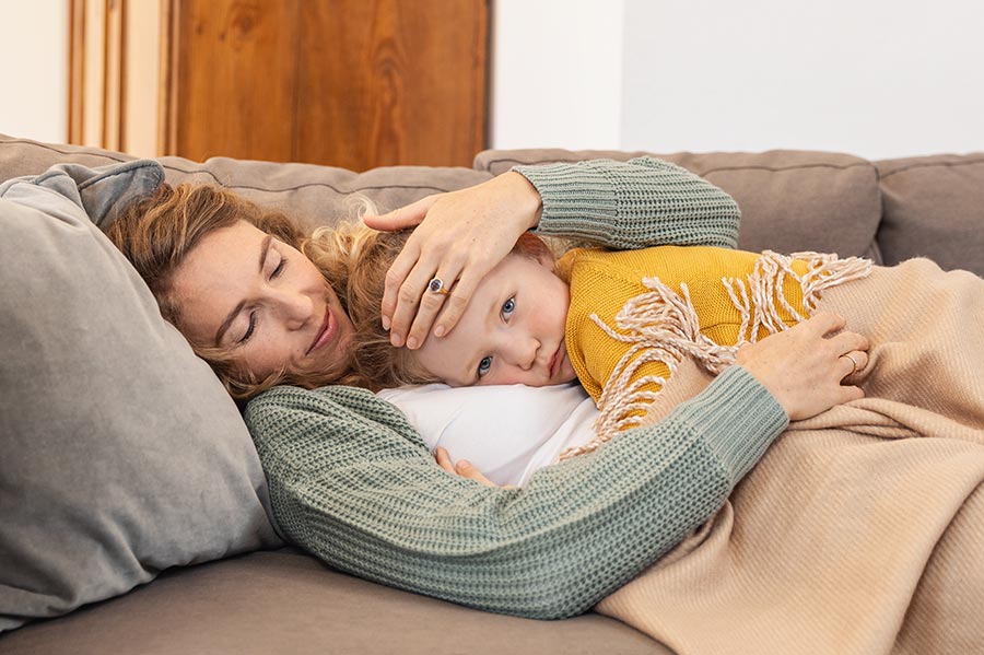 A sick girl lies in her mother's arms on the sofa